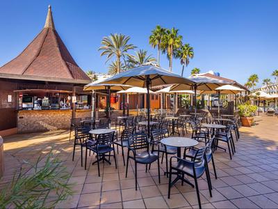 Außenbereich eines Hotels mit Tischen, Stühlen und Sonnenschirmen unter blauem Himmel.