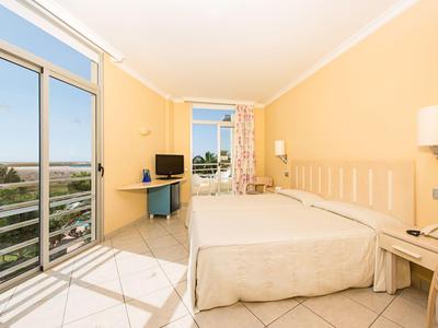 Habitación de hotel luminosa con cama doble, balcón y vista al mar.