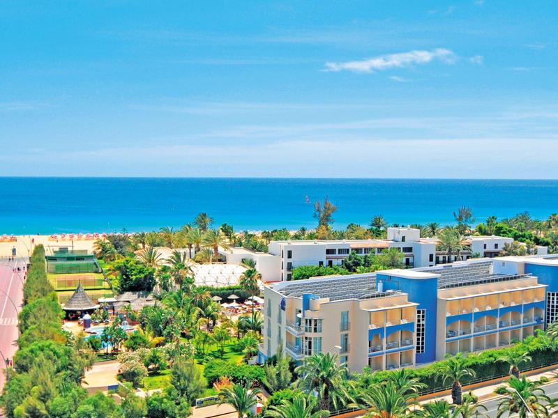 View of a modern coastal hotel with garden and sea in the background.
