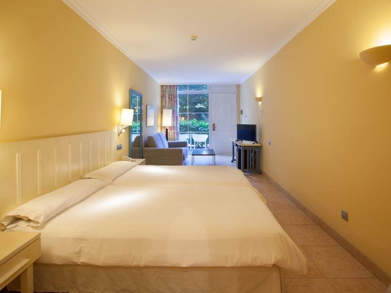 Bright hotel room with large bed, seating area, and terrace view.