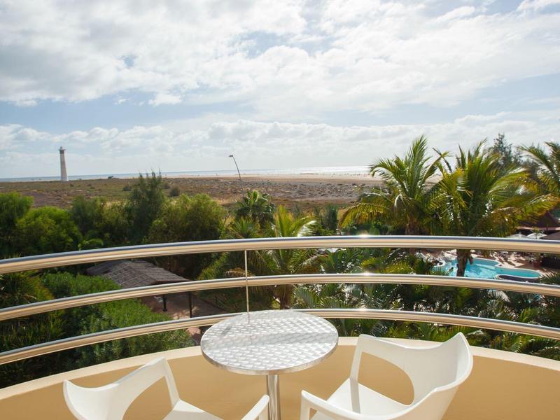 Balcony with three white chairs and small table overlooking the sea and palm trees.