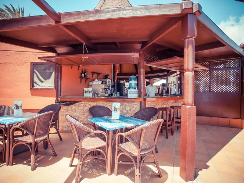 Outdoor bar area with tables and chairs under a wooden pavilion on a sunny day
