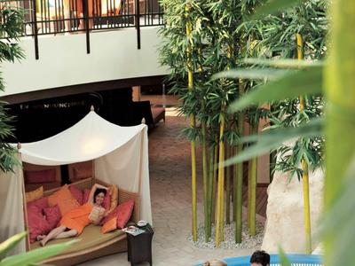 Hotel-Lobby mit tropischen Pflanzen, Lounge-Bereich und Gästen im Pool.