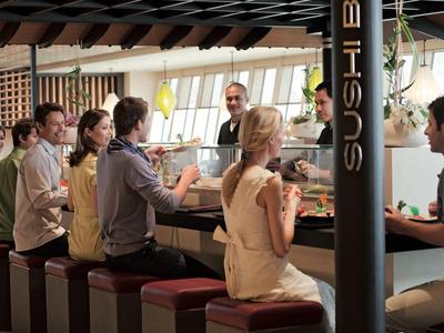 Menschen sitzen an einer Sushi-Bar in einem modern eingerichteten Hotelrestaurant.