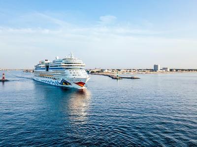 Ein großes Kreuzfahrtschiff fährt in ruhigem blauen Wasser unter einem klaren Himmel.
