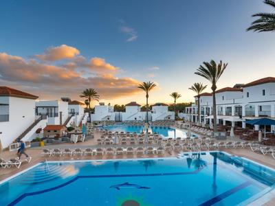 Area piscina dell'hotel al tramonto con palme e sedie a sdraio.