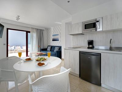 Moderner Küchen- und Essbereich mit weißen Möbeln, großer Fensterfront und Blick ins Freie.