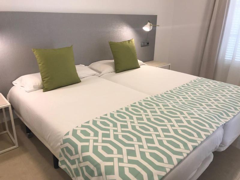 Ein großes Doppelbett mit weißer Bettwäsche, zwei grünen Kissen und einer gemusterten Tagesdecke.