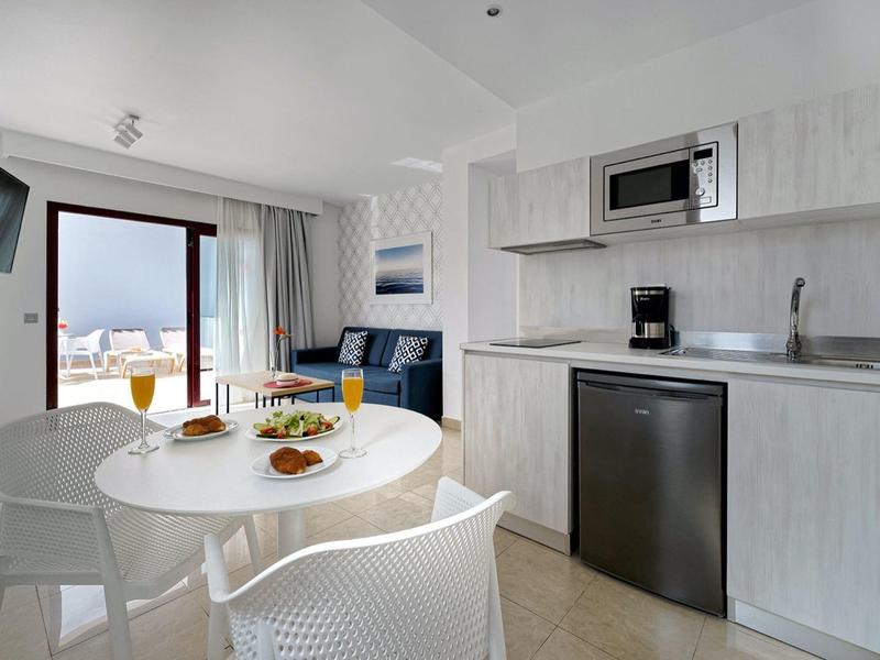 Moderner Küchen- und Essbereich mit weißen Möbeln, großer Fensterfront und Blick ins Freie.