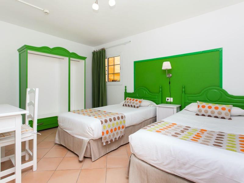 Hotelkamer met twee eenpersoonsbedden, groene hoofdeinden, kledingkast en bureau.