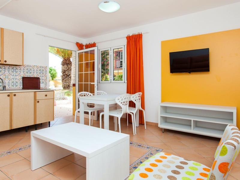 Lichte woonruimte met oranje accenten, tv, eethoek, kitchenette en toegang tot terras.