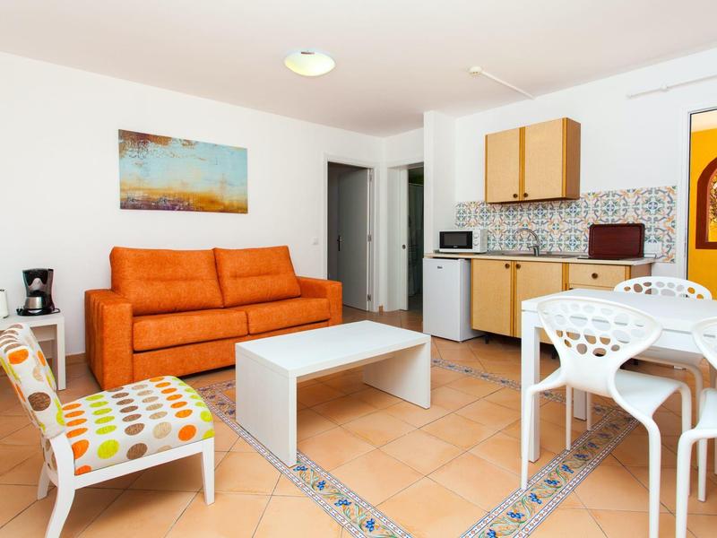 Modern ingerichte woonkamer met oranje bank, witte tafel en kitchenette.
