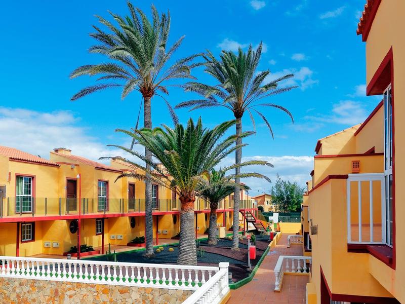 Zonnig hotelcomplex met gele gebouwen en hoge palmbomen onder een heldere blauwe lucht.