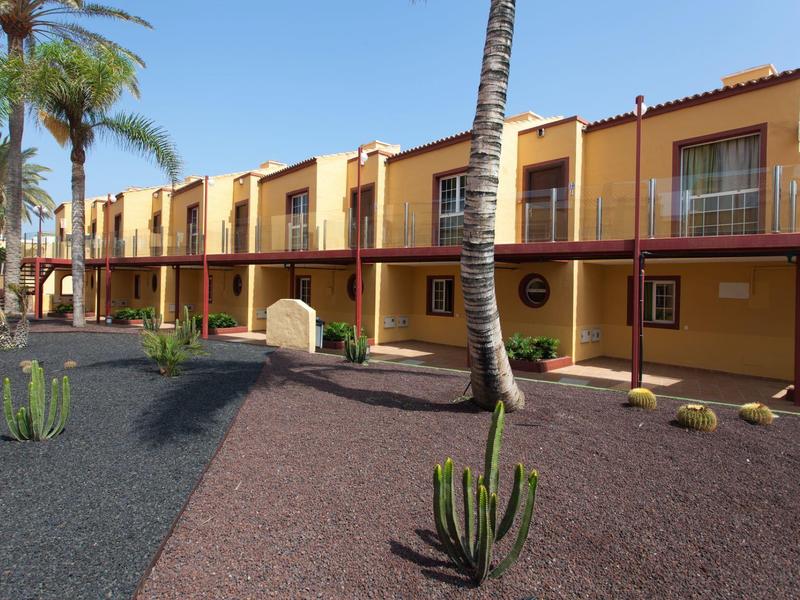 Geel hotelgebouw met balkons en omliggend woestijnachtig landschap