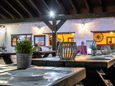 Rustiek restaurant met houten tafels, decoratieve kandelaar en planten in potten.