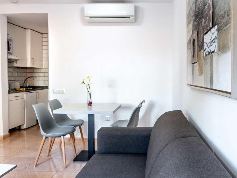 Modern living area with gray sofa, dining table, chairs, and open kitchen.