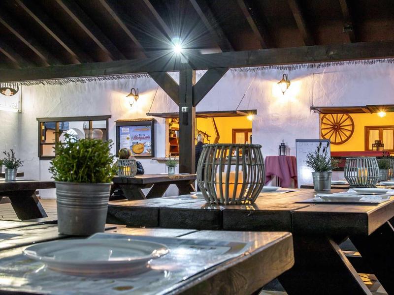 Rustic outdoor tables in front of a whitewashed building with wooden beams and decorative wagon wheels.