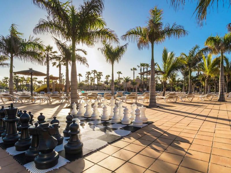 Large outdoor chess set among palm trees on sunny terrace at a resort
