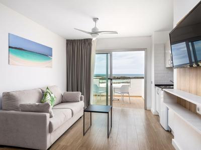 Salon moderne avec canapé gris, table en verre et balcon avec vue sur la mer.