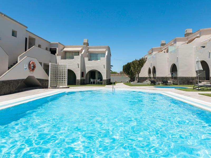 Ein großer blauer Pool vor weißen Wohnhäusern unter klarem Himmel.