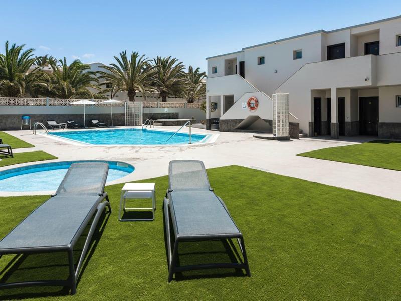 Modernes Wohnhaus mit Schwimmbad, grüner Rasenfläche und Liegestühlen bei klarem Himmel.