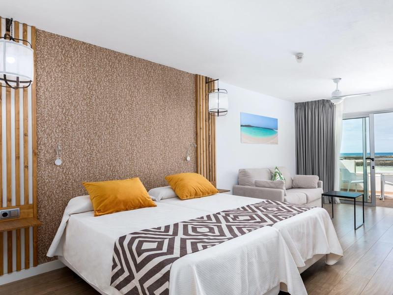 Hell eingerichtetes Schlafzimmer mit großem Bett, bunten Kissen und Balkon mit Meerblick.