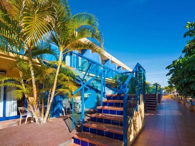 Außenbereich eines Hotels mit blauen Treppen, Palmen und sonnigem Himmel.