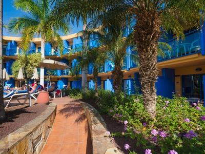 Hotelgarten mit Palmen, blühenden Pflanzen und Sitzbereichen unter blauem Himmel.