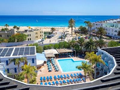 Hotel mit Pool und Liegestühlen, umgeben von Palmen nahe am Strand und Meer.