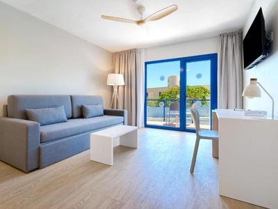 Hell eingerichtetes Hotelzimmer mit Sofa, Schreibtisch und Balkon mit Ausblick.
