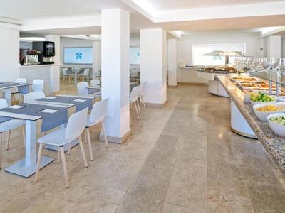 Modernes, helles Hotelrestaurant mit Buffet und Sitzbereich mit weißen Stühlen und Tischen.