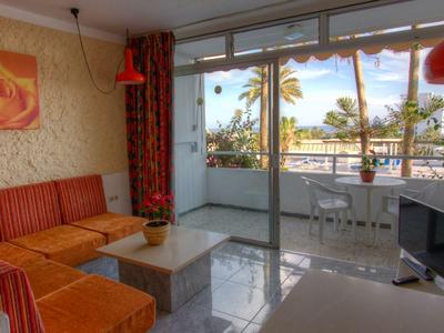 Soggiorno luminoso con divano rosso e accesso al balcone con vista sul mare e palme.