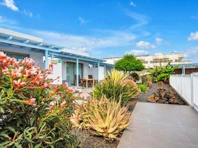 Moderner Bungalow mit Terrasse, blühenden Pflanzen und klarem Himmel im Hintergrund.