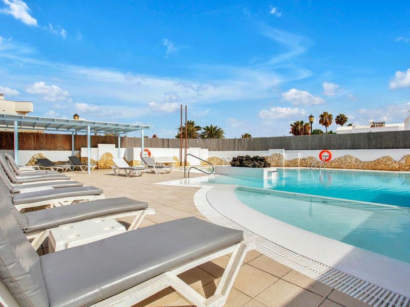 Modern outdoor pool with sun loungers and sunny blue sky at a hotel.