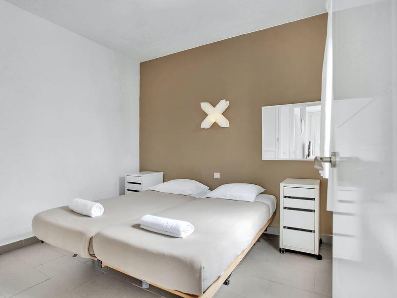 Modern hotel room with two single beds, nightstands, and minimalist design.