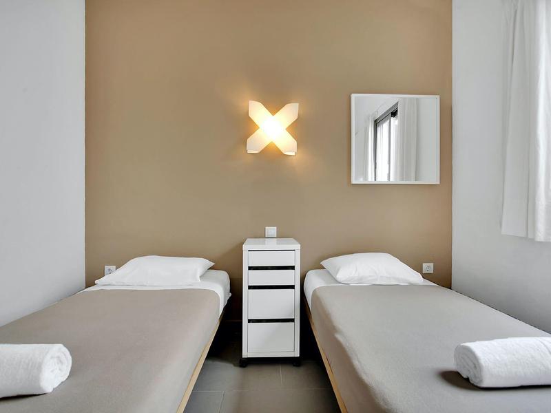 Hotel room with two single beds, nightstand, and modern wall light.