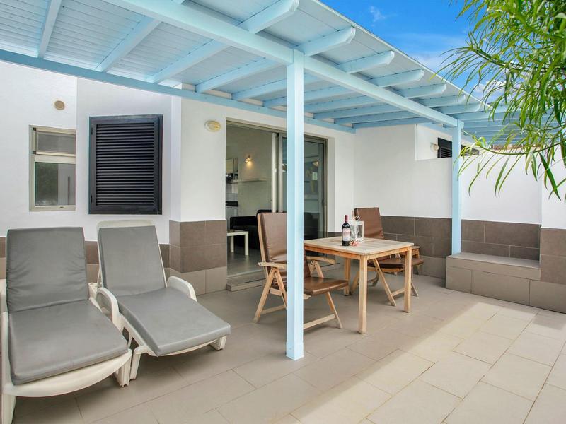 Covered patio with lounge chairs, dining table, and sofa beside a white building.