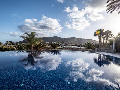 Una piscina tranquila refleja palmeras y el cielo en un resort tropical.