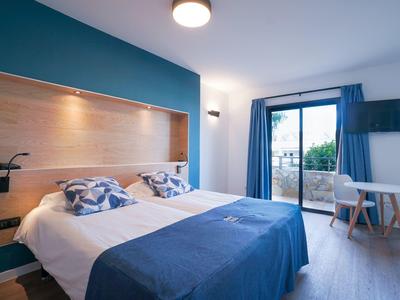 Camera d'hotel luminosa con letto matrimoniale, biancheria blu-bianca e accesso al balcone.