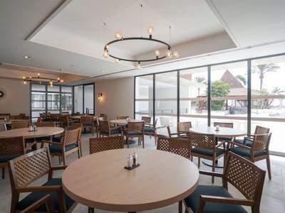 Comedor luminoso con mesas redondas y sillas de madera junto a grandes ventanas con vista al exterior.