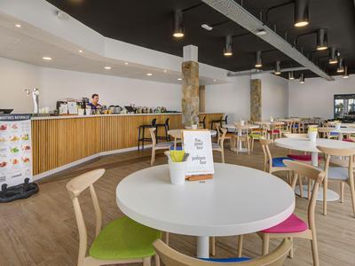 Sala de café moderna con mesas, sillas coloridas y largo mostrador de madera clara.