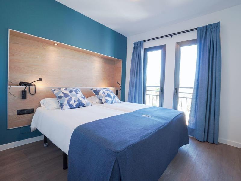 Camera d'hotel moderna con letto matrimoniale, pareti blu, tende e porte balcone.