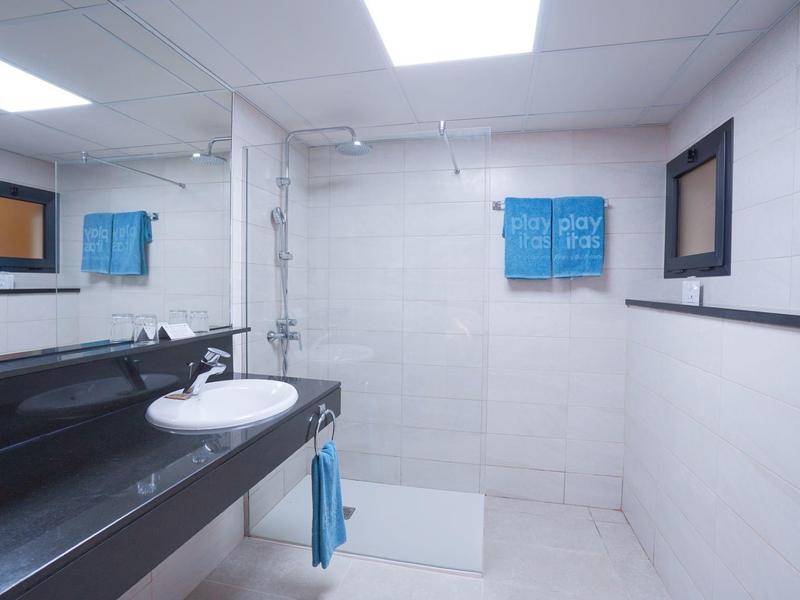 Bagno moderno con pareti piastrellate bianche, grande specchio e piano lavabo nero.