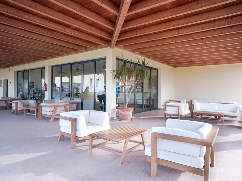 Terrazza esterna coperta con aree salotto accoglienti e mobili in legno davanti a grandi finestre in vetro.