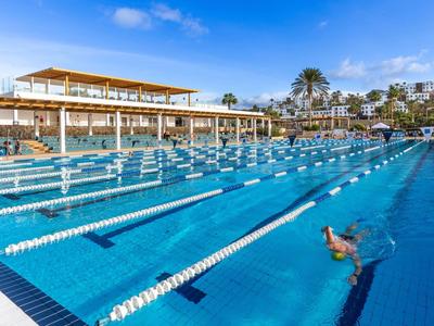 Large outdoor pool with swimming lanes and a swimmer in a sunny hotel setting.