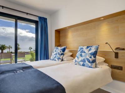 Moderne hotelkamer met twee eenpersoonsbedden, blauw beddengoed en terras met uitzicht op groen gras.