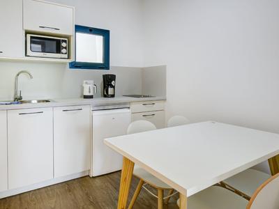 Moderne, minimalistische kitchenette met witte tafel en stoelen in een hotelkamer.