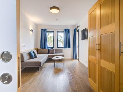 Uitzicht op een lichte hotelkamer met bank, tafel en grote ramen met blauwe gordijnen.