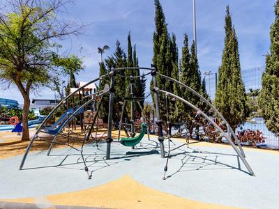 Modern speelterrein met glijbaan, schommels en klimrek onder een heldere hemel.