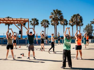 Group of people doing outdoor gymnastics on a sunny day with palm trees in the background.